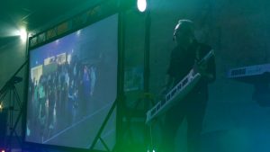 DJ animateur sur scène avec clavier et écran vidéo géant lors d’une soirée dansante avec animation musicale et visuelle.