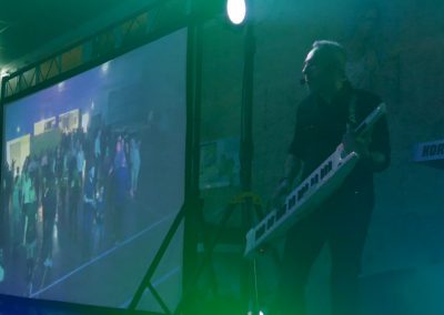 DJ animateur sur scène avec clavier et écran vidéo géant lors d’une soirée dansante avec animation musicale et visuelle.