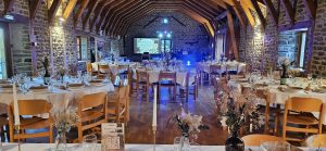 Installation DJ pour un mariage dans une salle en pierre, avec écran vidéo, éclairage d’ambiance et tables dressées.