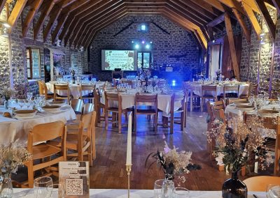 Installation DJ pour un mariage dans une salle en pierre, avec écran vidéo, éclairage d’ambiance et tables dressées.